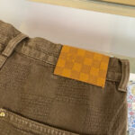 Pantaloni marroni eleganti con etichetta a quadri e bottoni metallici, stile moda sofisticata.