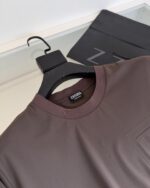 Maglietta minimalista in tonalità terra con taschino, su appendiabiti nero con logo Z.