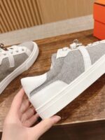 Sneakers moderne grigie e bianche low-top con dettagli eleganti, su superficie in legno luminosa.