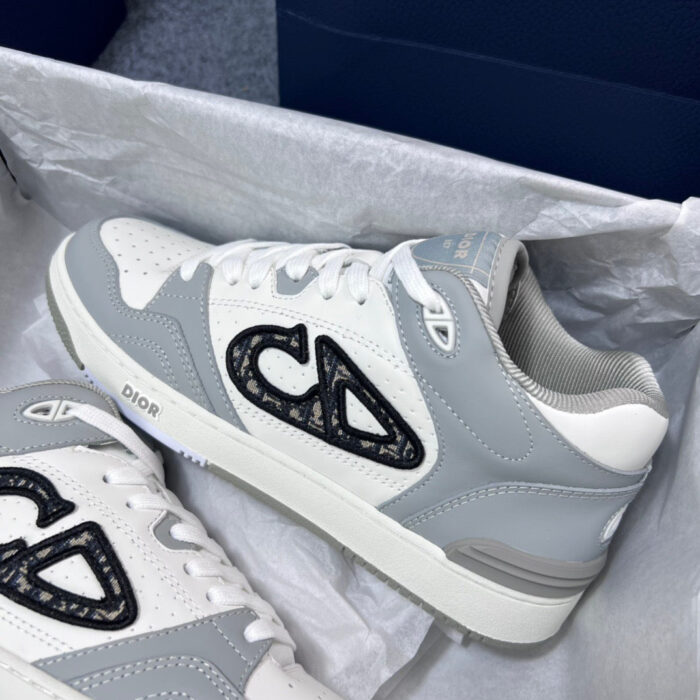 Sneakers moderne grigie e bianche con logo nero, stile sporty e trendy, su sfondo blu.