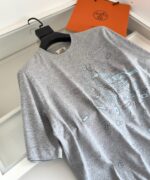 Maglietta grigia moderna con grafiche astratte, di qualità, accompagnata da borsa arancione elegante.