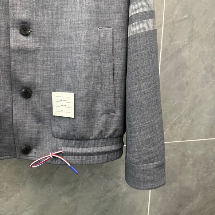 Giacca moderna grigia con bottoni, dettagli a strisce e cordino regolabile multicolore.