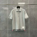 Maglietta polo grigia con strisce bianche, logo sul lato e design sportivo elegante.