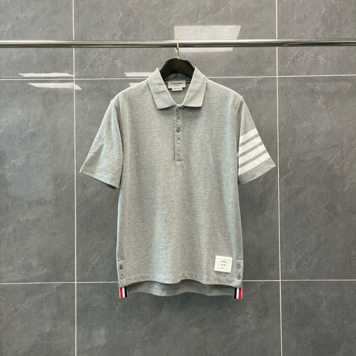 Maglietta polo grigia con strisce bianche, logo sul lato e design sportivo elegante.