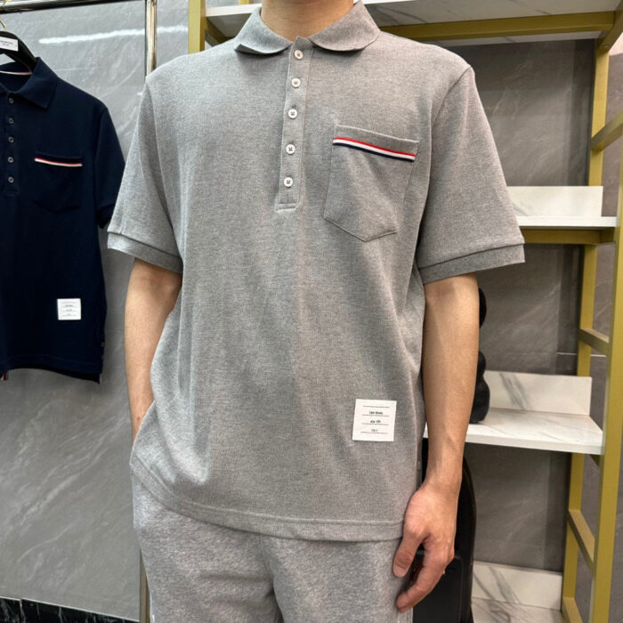 Maglietta polo grigia con dettaglio colorato sulla tasca, stile casual e moderno.