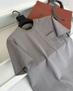 Maglietta grigia elegante con borsa shopping marrone e manici azzurri, stile minimalista e raffinato.