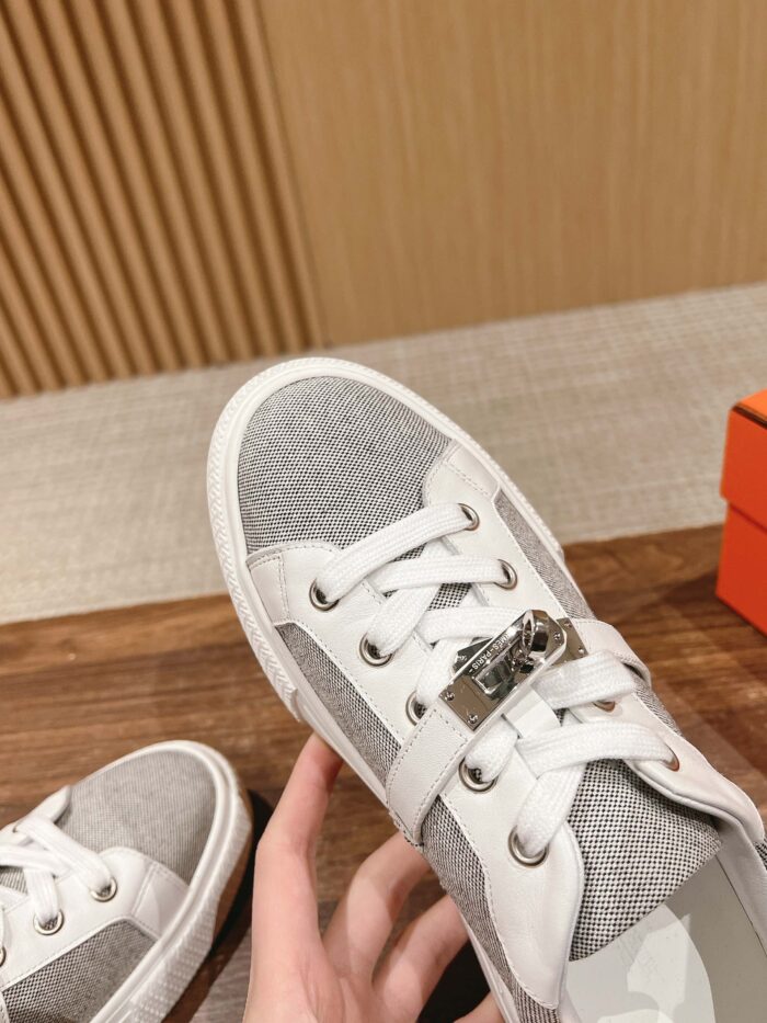 Scarpa sneaker moderna grigia e bianca con dettaglio in metallo, stile casual e confortevole.