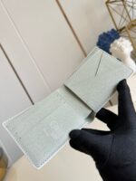 Portafoglio in pelle verde menta con scomparti eleganti, tenuto in mano con guanto raffinato.