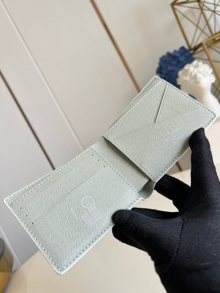 Portafoglio in pelle verde menta con scomparti eleganti, tenuto in mano con guanto raffinato.