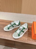Sneakers verde chiaro e bianco su superficie in legno, con scatola arancione elegante e design moderno.