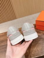 Sneaker grigia in pelle con dettaglio rosa, in primo piano su sfondo in legno e scatola arancione.