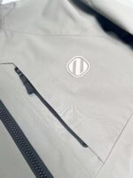 Giacca grigia minimalista con logo bianco e tasca zippata, stile moderno e funzionale.