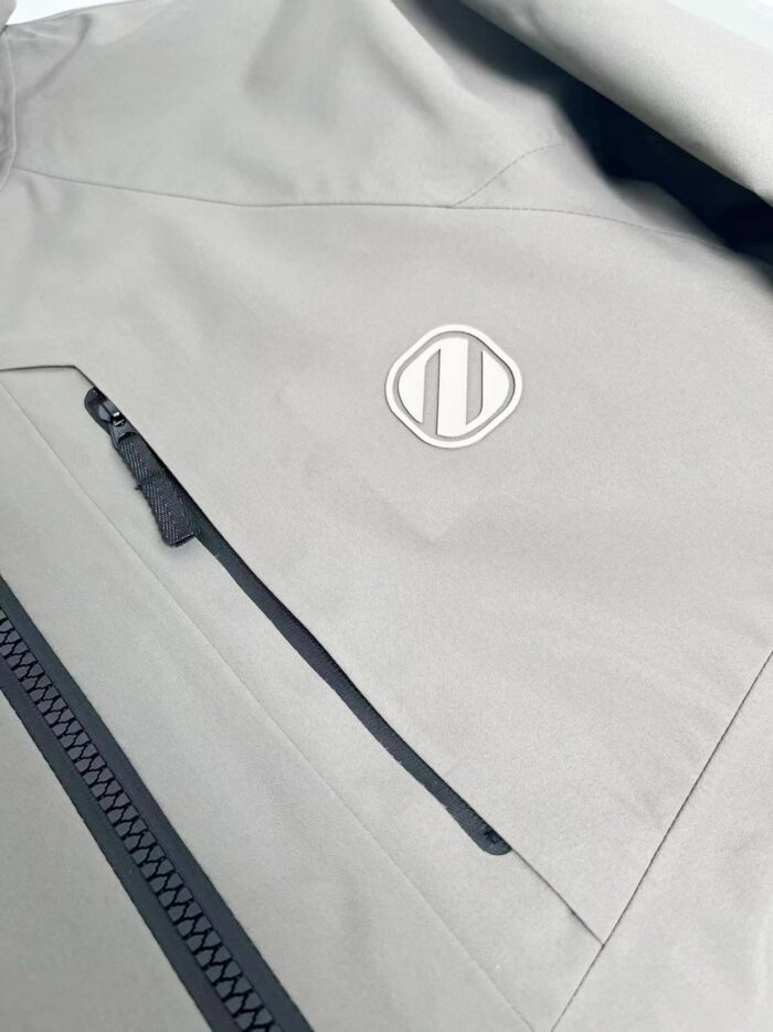 Giacca grigia minimalista con logo bianco e tasca zippata, stile moderno e funzionale.