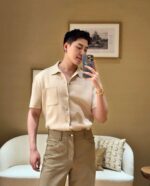 Uomo in selfie con abbigliamento beige, salotto elegante e arte moderna sullo sfondo.