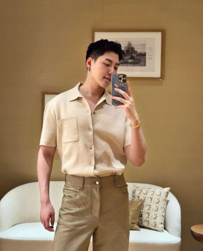 Uomo in selfie con abbigliamento beige, salotto elegante e arte moderna sullo sfondo.