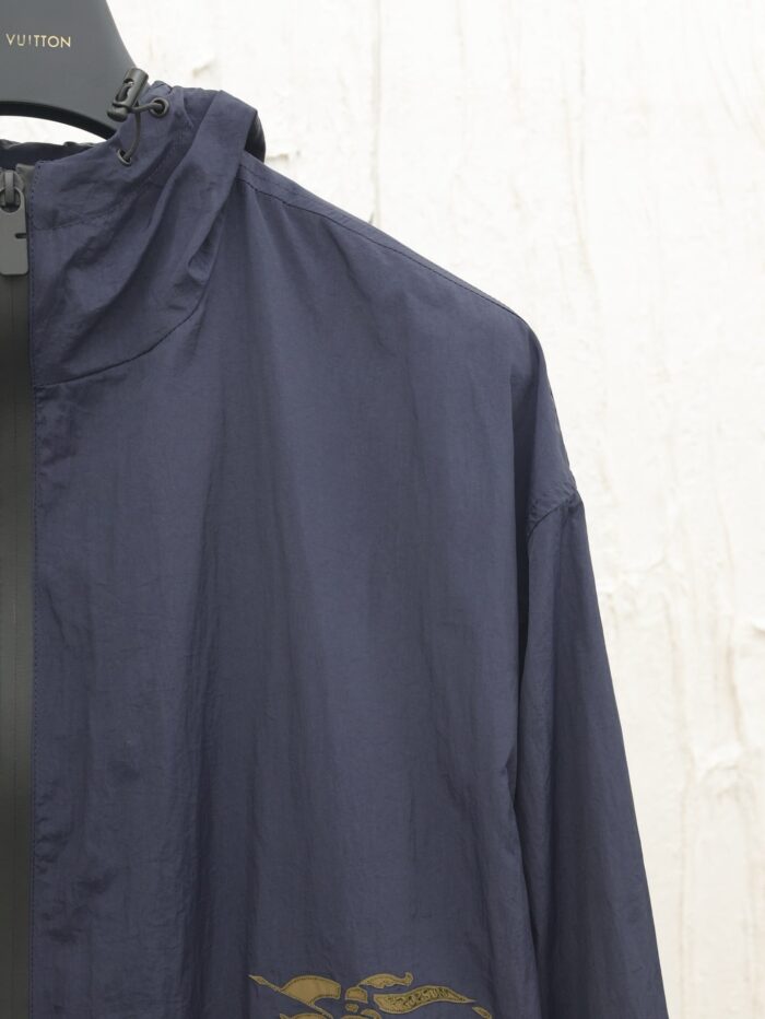 Giacca leggero navy con logo dorato e cappuccio invisibile, stile casual e pratico.