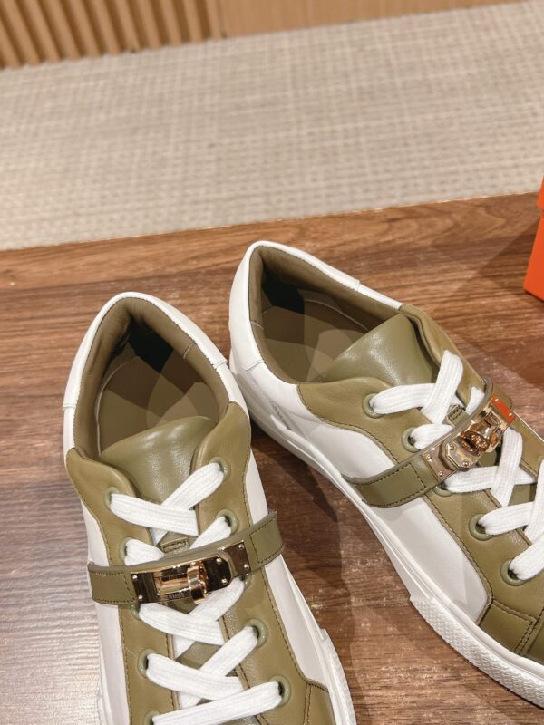 Scarpe sneaker eleganti verde oliva e bianco con cinturino dorato, su superficie di legno.