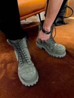 Persona che allaccia stivali militari verdi in ambiente accogliente con divano arancione.