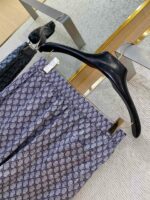 Pantaloni eleganti interlacciati navy e crema su appendiabiti moderno, tessuto lucido di alta qualità.