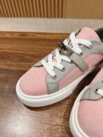 Sneakers rosa e grigie in tessuto con fibbia e suola bianca su superficie in legno.