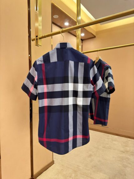 Camicia a quadri blu navy, bianco e rosso su appendiabiti dorato in ambiente elegante.