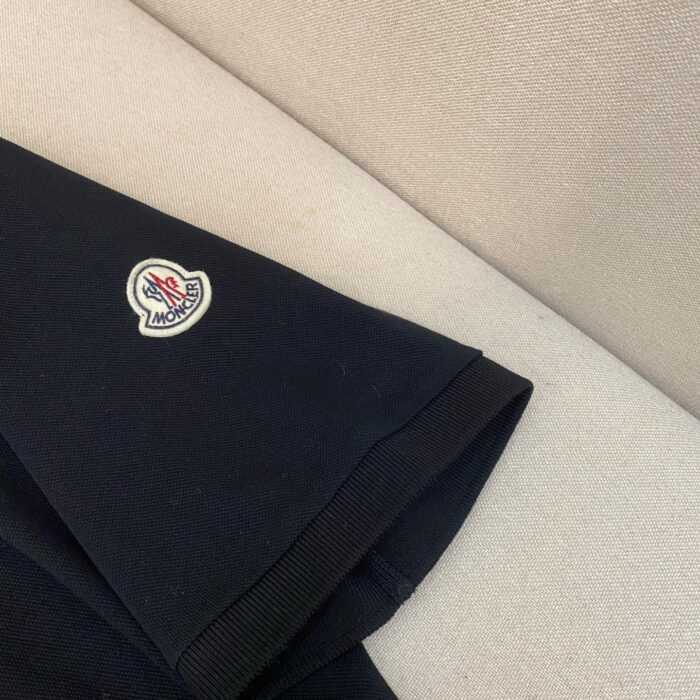 Manica di giacca scura con logo circolare bianco e rosso, stile elegante e minimalista.