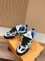 Sneakers sportive in bianco, nero e blu con logo e scatola arancione su superficie in legno.