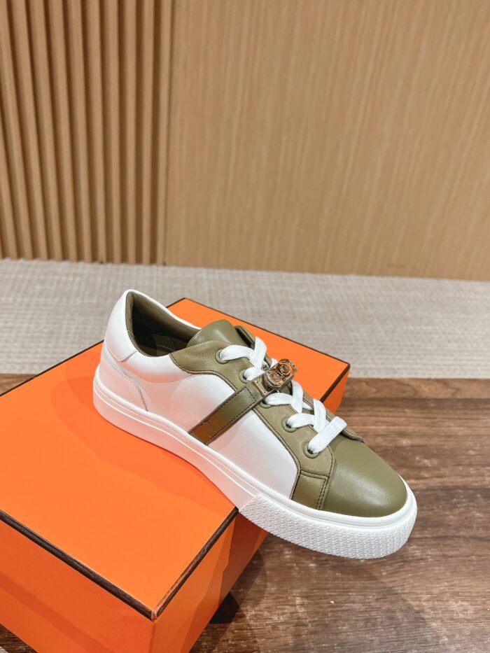 Sneaker elegante bianca e verde oliva su scatola arancione, stile moderno e di qualità.