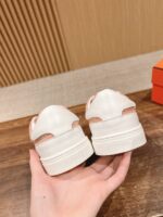 Sneakers bianche con dettagli rosa, tenute in mano su tavolo di legno, sfondo con parete di listelli.