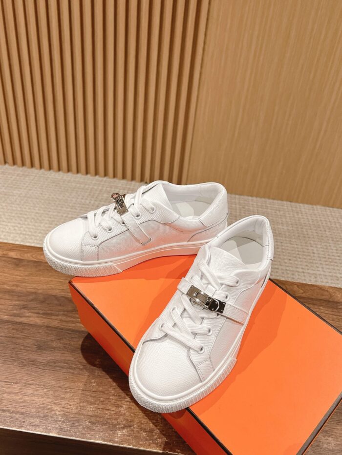 Sneaker bianche moderne con dettaglio metallico su scatola arancione in ambiente trendy e raffinato.