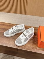 Sneaker bianche moderne con dettagli metallici su superficie in legno e scatola arancione elegante.