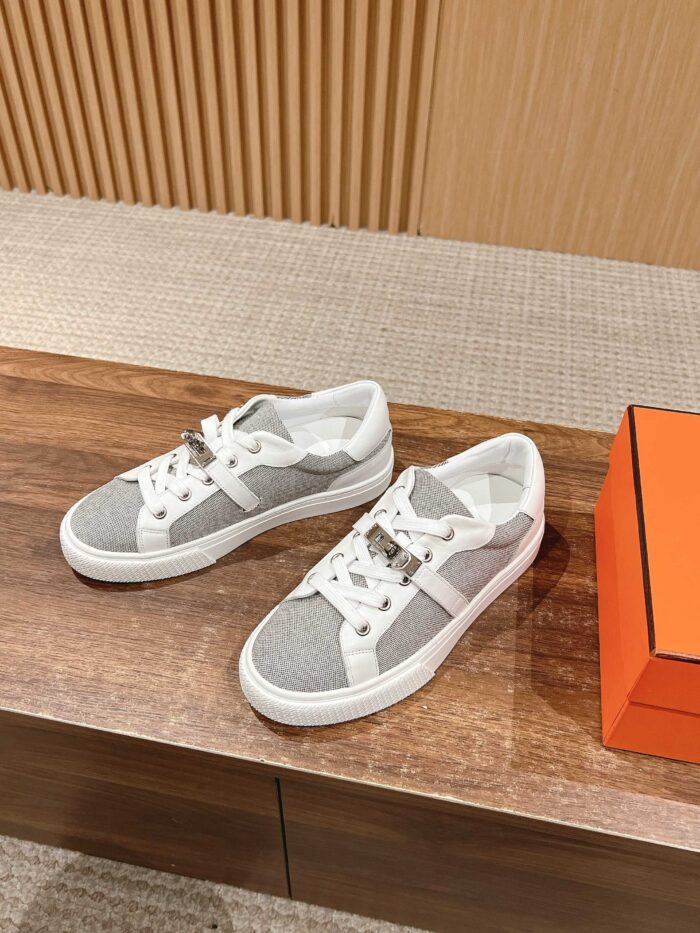 Sneaker bianche moderne con dettagli metallici su superficie in legno e scatola arancione elegante.