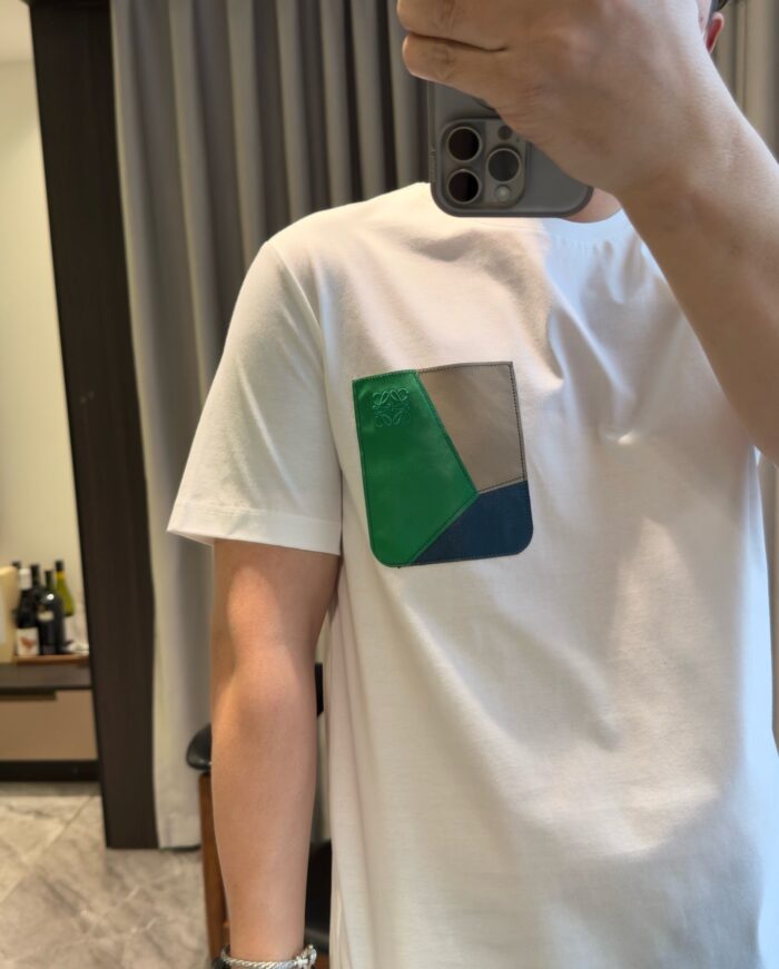 Maglietta bianca con tasca colorata, stile casual, dettaglio moderno, selfie in ambiente luminoso.