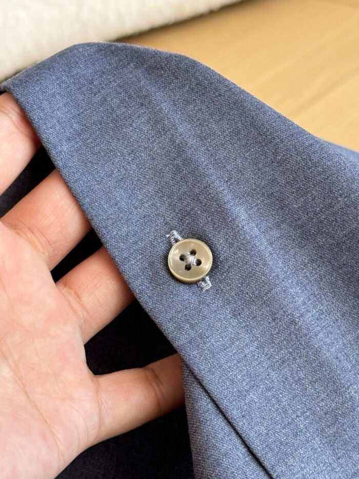 Dettaglio del polsino di giacca elegante con bottone in tessuto grigio raffinato.