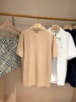 Abbigliamento estivo con polo beige, bianca e pantaloncini a quadri su appendini in legno.