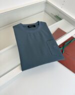 Maglietta minimalista in blu petrolio su superficie in legno con sacchetto rosso-marrone.