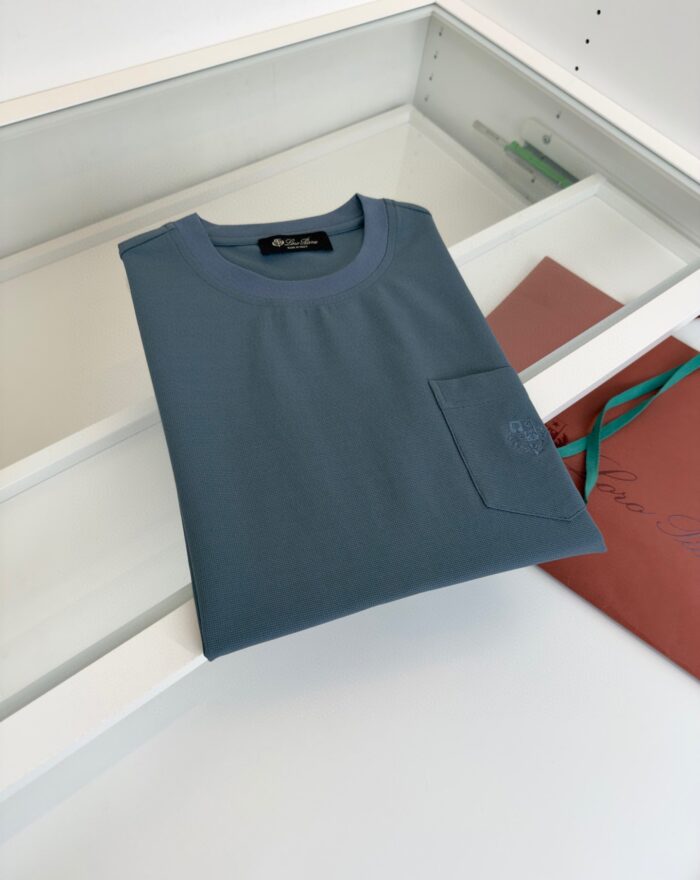 Maglietta minimalista in blu petrolio su superficie in legno con sacchetto rosso-marrone.