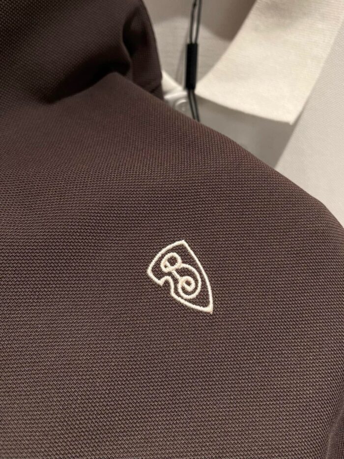 Tessuto marrone scuro con logo bianco moderno e texture resistente, ideale per accessori di moda.