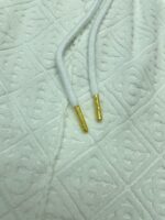 Cordini dorati su tessuto quilted bianco, elegante dettaglio di moda casual e di qualità.