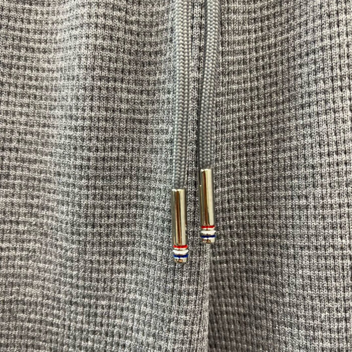 Dettaglio di tessuto grigio e cerniera con inserti sportivi e finiture eleganti.