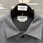 Camicia grigia Thom Browne con etichette di lusso, dettaglio di collare e materiali di alta qualità.