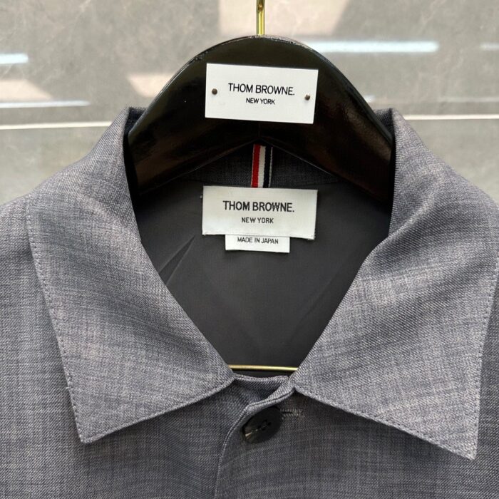 Camicia grigia Thom Browne con etichette di lusso, dettaglio di collare e materiali di alta qualità.
