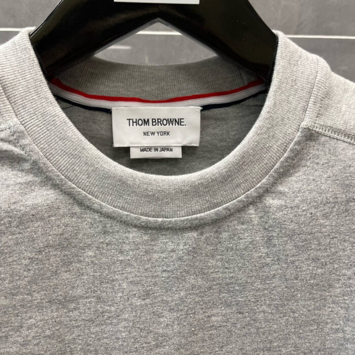Maglia grigia Thom Browne con logo, dettaglio colorato e qualità Made in Japan.