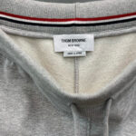 Maglione Thom Browne grigio con dettaglio rigato, logo discreto e cuciture di alta qualità.