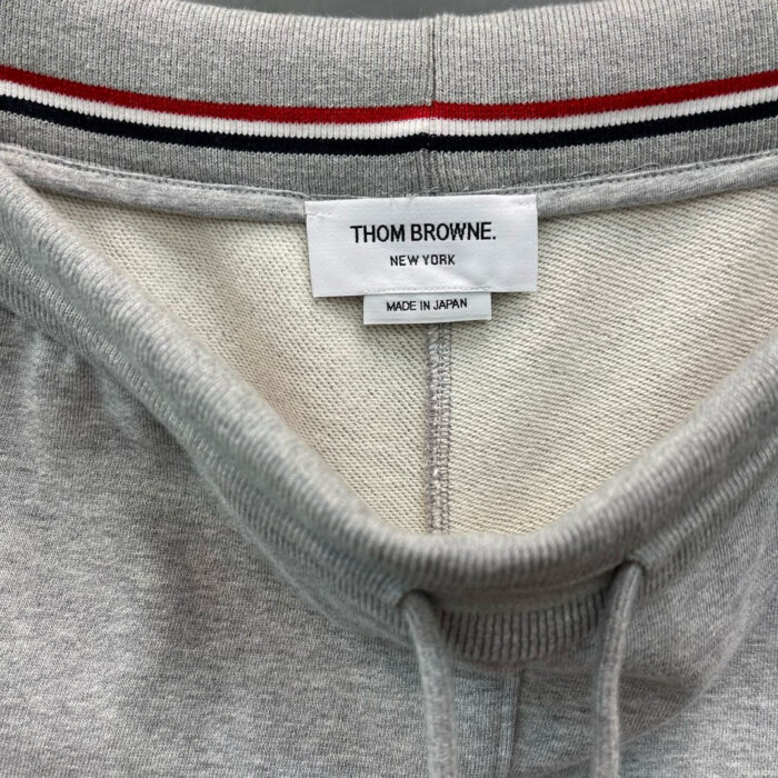 Maglione Thom Browne grigio con dettaglio rigato, logo discreto e cuciture di alta qualità.