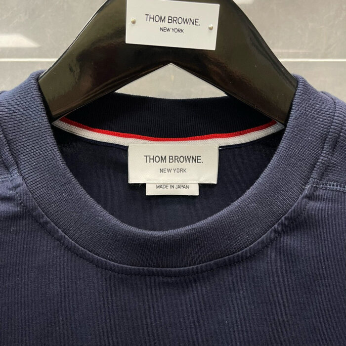 Etichetta Thom Browne navy made in Japan con dettaglio a strisce sul colletto.