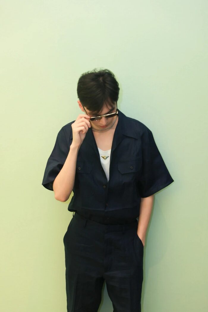 Ragazzo in abbigliamento navy sognante davanti a parete verde pastello, stile minimalista moderno.