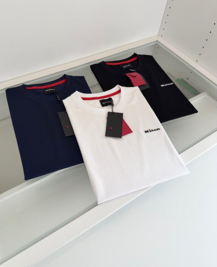 Esposizione di T-shirt minimaliste in bianco, navy e nero con dettagli rossi su tavolo elegante.