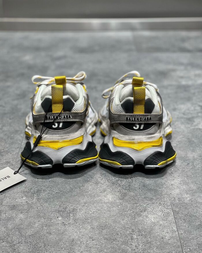 Sneakers moderne bianche con suola spessa, dettagli gialli e design streetwear di tendenza.