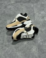 Sneakers streetwear beige e nero, design chunky e dettagli moderni su superficie grigia.